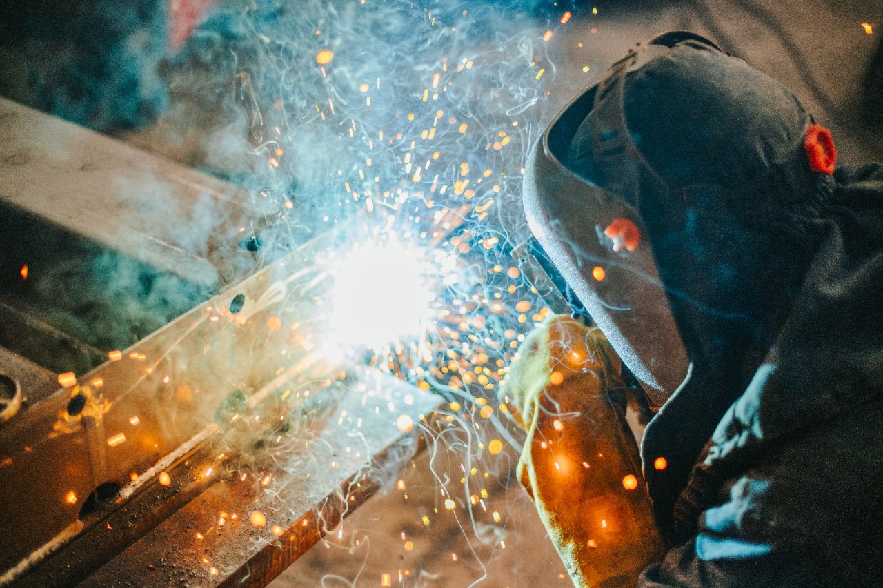 Ein Schweißer trägt eine Schutzausrüstung, während er zwei Metallteile miteinander verbindet.