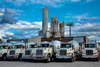A range of cement mixer trucks  in a parking lot of a cement factiry.